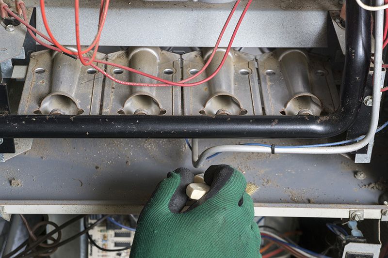 Someone working on furnace with green gloves. 5 Reasons to Schedule a Fall Furnace Clean and Check.